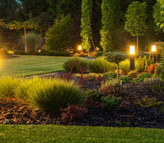Panoramic Photo of LED Light Posts Illuminated Backyard Garden During Night Hours. Modern Backyard Outdoor Lighting Systems.